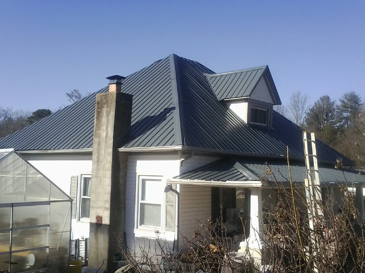 Dark blue standing seam metal roof on a white farmhouse with dormer — Slate & Tile Roof Repair by Roofing Brothers in Havensville