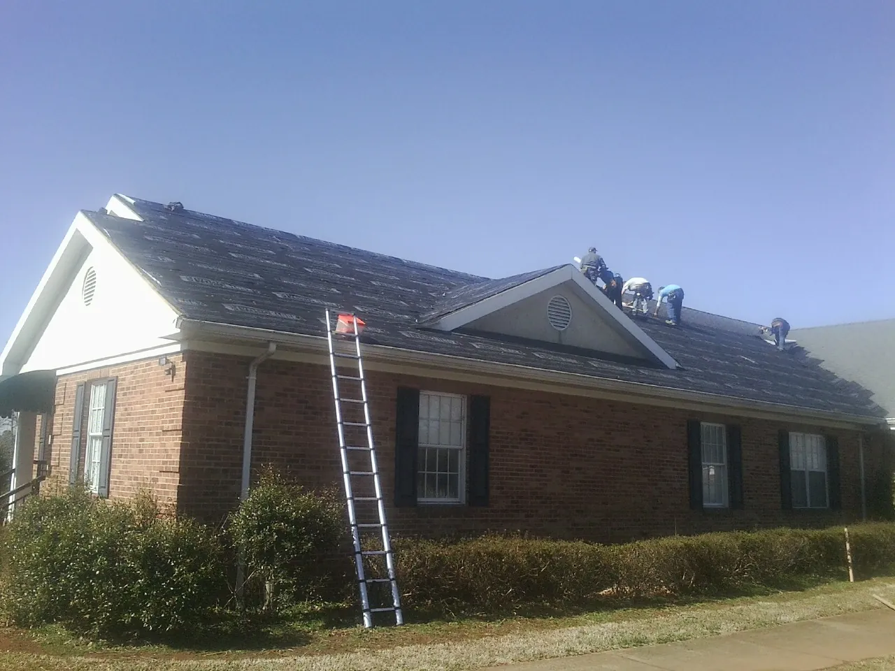 Crew tearing shingles off a brick ranch roof with a ladder set — Emergency Roof Repair work by our crew in Havensville