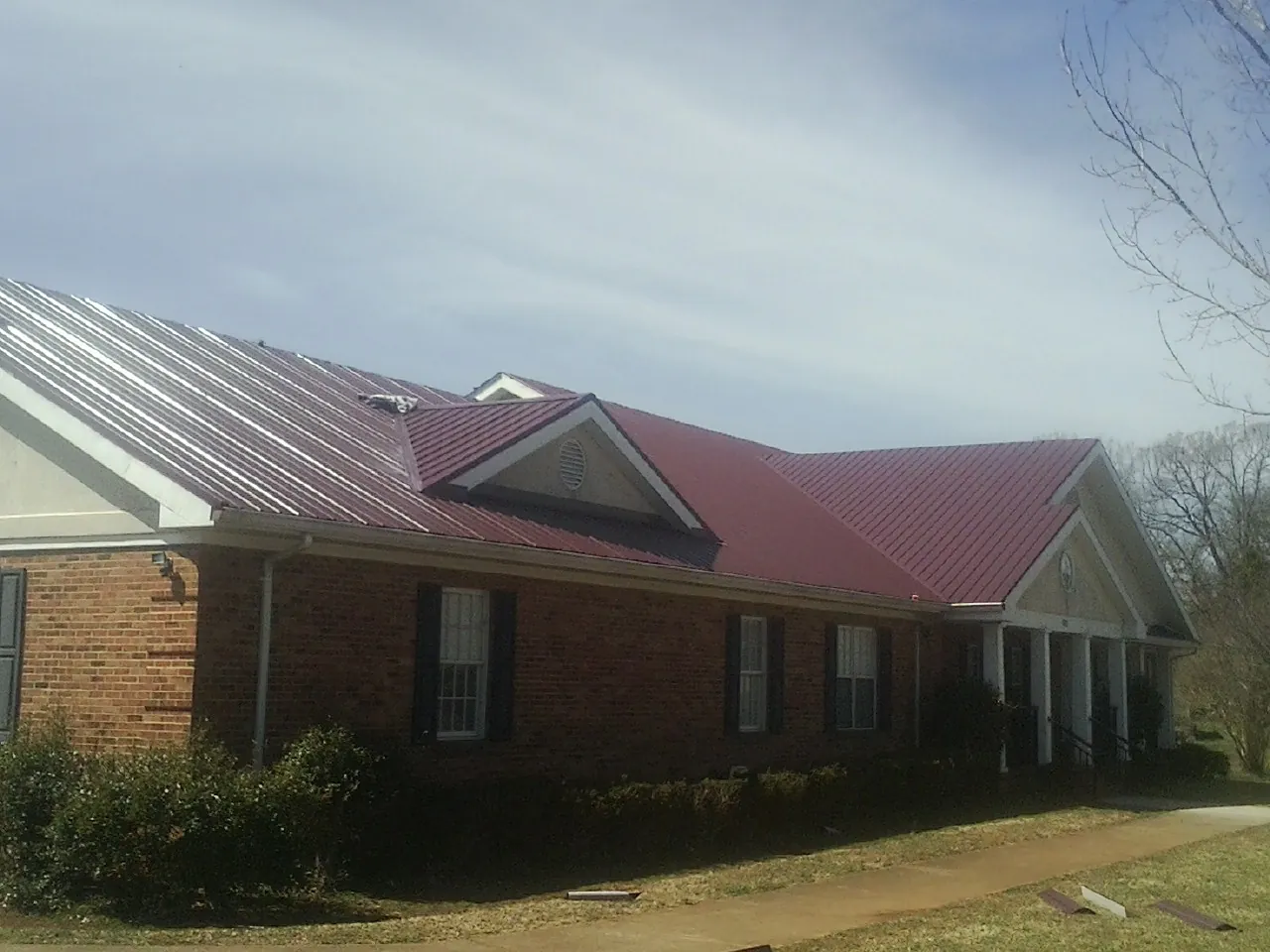 Red metal roof with gabled entries on a long brick building, from a Hail Damage Roof Repair job in Havensville