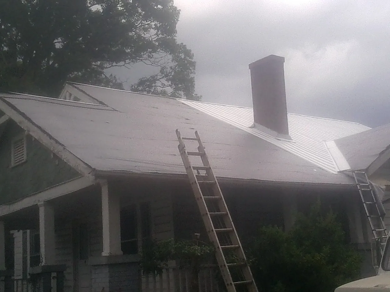 Ladders against a metal roof on an older home with a brick chimney in Havensville