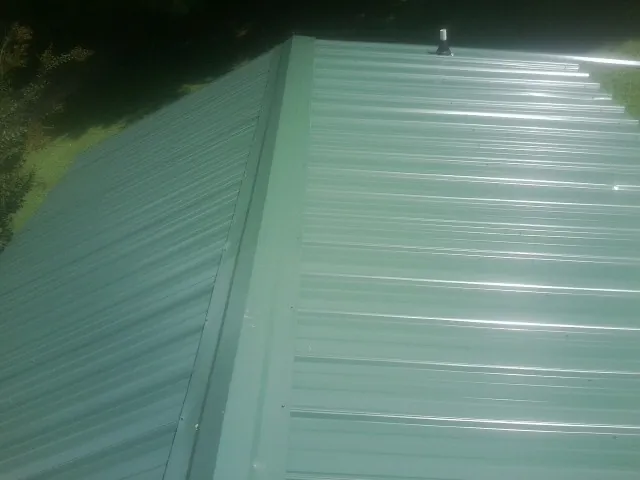 New green metal panels meeting at the ridge of a roof — Flat Roof Repair work by our crew in Havensville