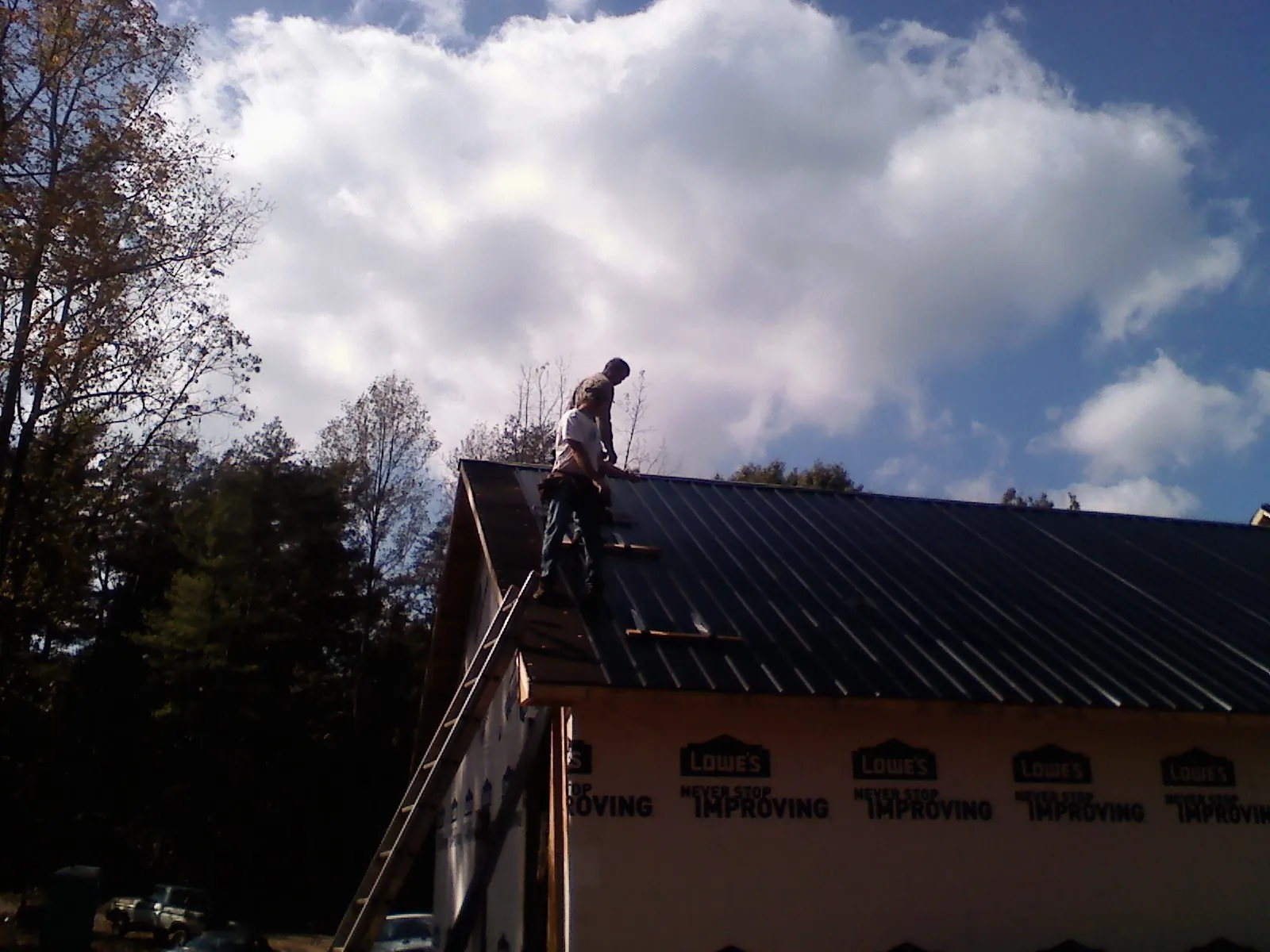 Roofer fastening dark metal panels high against a cloudy sky, from a Roof Inspection job in Havensville