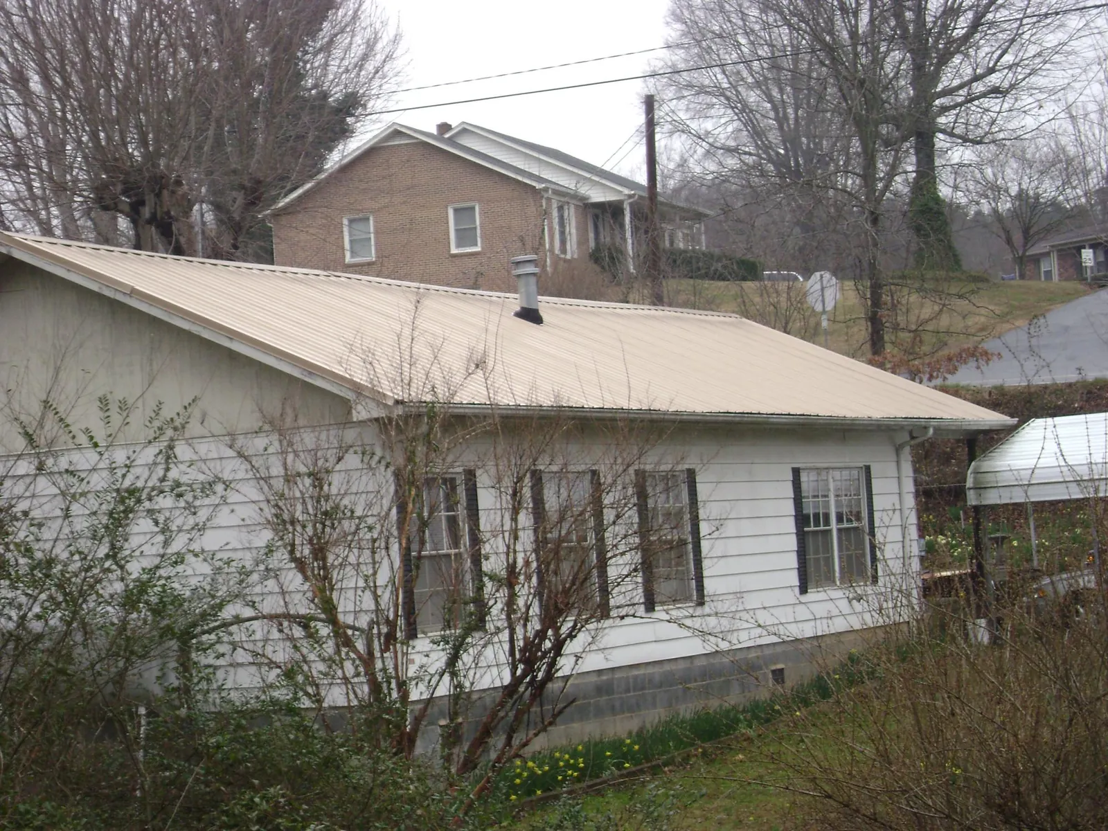 Tan metal roof on a white sided house set into a hillside — Commercial Roofing by Roofing Brothers in Havensville